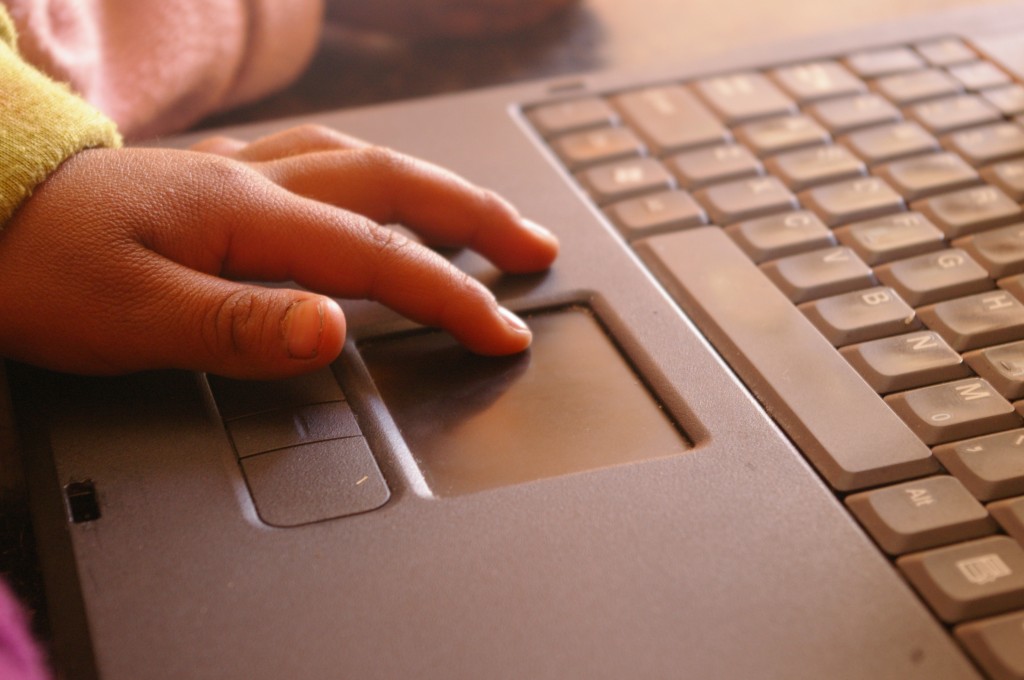 A child's hand poised on the trackpad of a laptop.