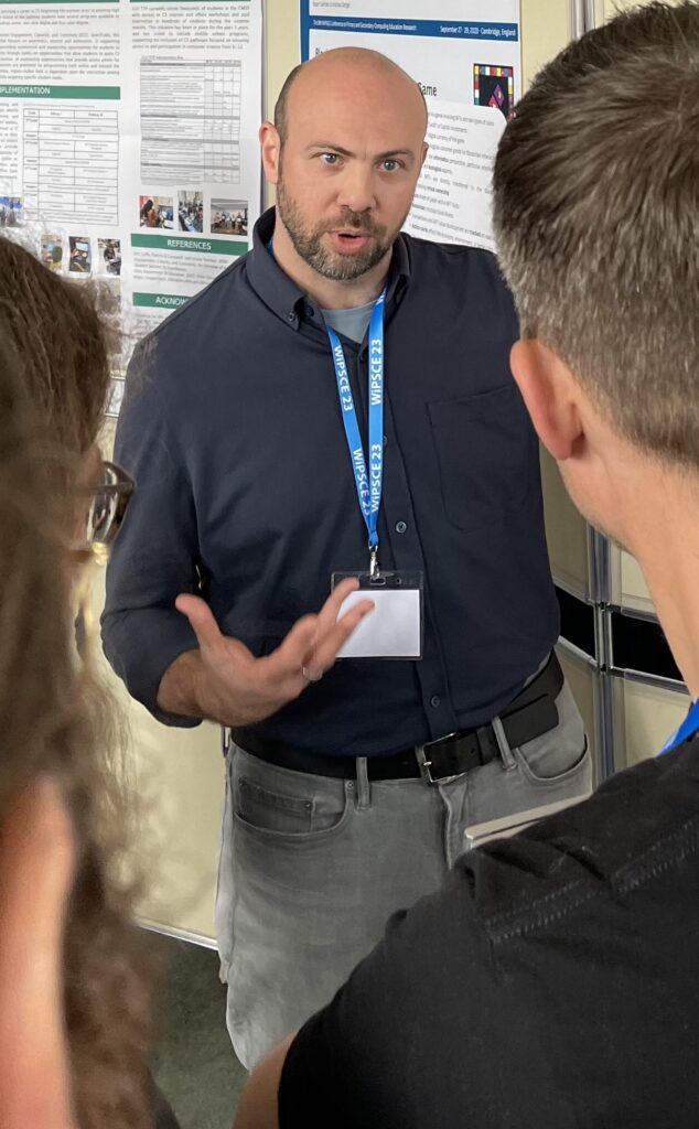 Mike Deutsch photographed discussing his research poster with attendees, at WiPSCE 2023 (September 2023, Cambridge, UK).